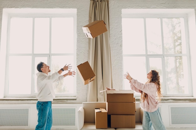 Un jeune couple de famille heureuse, un homme et une femme, jettent des boîtes de carton sur leur nouvelle maison.