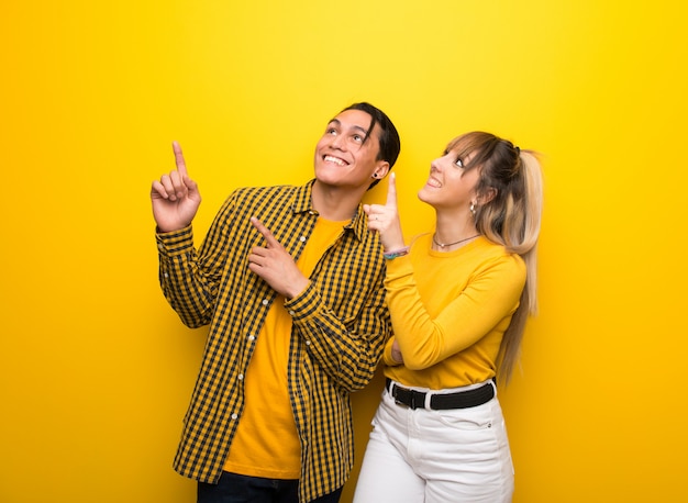 Jeune couple sur fond jaune vibrant pointant avec l&#39;index