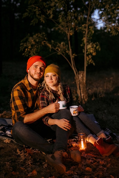 Jeune couple un gars et une fille dans des chapeaux tricotés lumineux s'est arrêté dans un camping près du feu