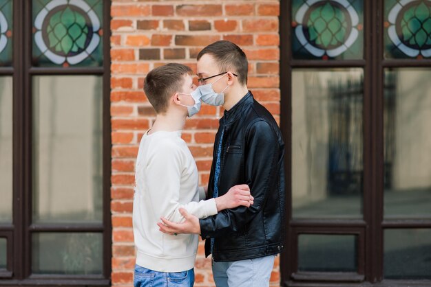 Jeune couple gay portant un masque médical, s'embrassant et s'embrassant dans la ville.