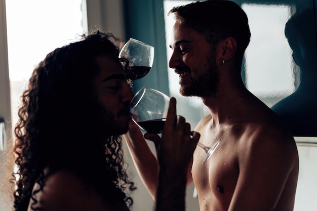 Jeune couple gay se détendre à l'intérieur en sirotant un verre de vin rouge photo rétroéclairée