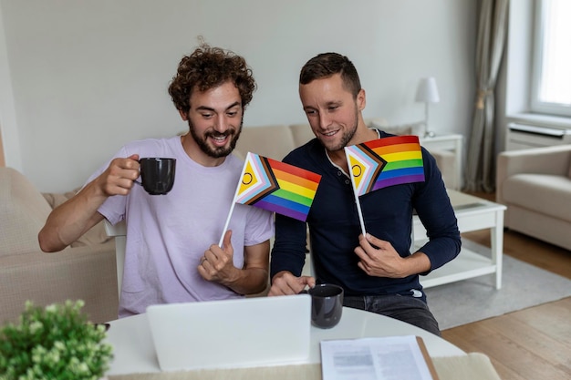 Jeune couple gay souriant joyeusement tout en saluant leurs amis lors d'un appel vidéo