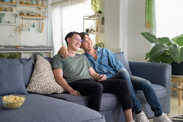 Jeune couple gay souriant regardant la télévision dans le salon à la maison LGBTQ et diversité