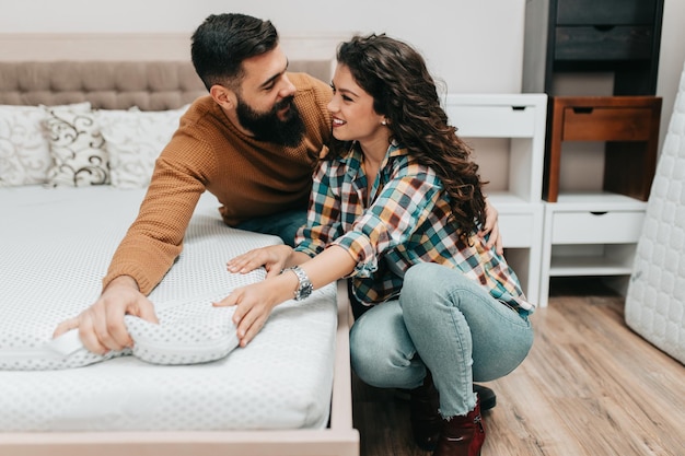 Jeune couple heureux achetant un nouveau lit et matelas dans un grand magasin de meubles