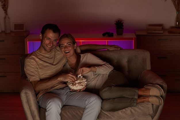 Jeune couple heureux allongé sur un canapé avec du pop-corn et regarder un film pendant les loisirs à la maison