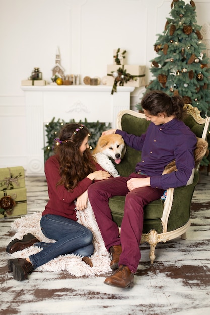 Jeune couple heureux câlins adorable chien akita inu tout en étant assis sur un élégant fauteuil rétro