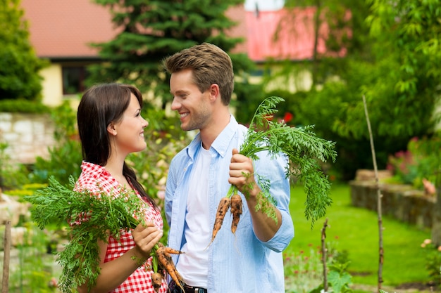 Jeune couple heureux avec les carottes de son jardin