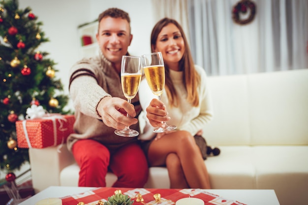 Un jeune couple heureux célébrant Noël avec des verres de champagne à leur domicile. Mise au point sélective. Concentrez-vous sur le premier plan, sur les lunettes.