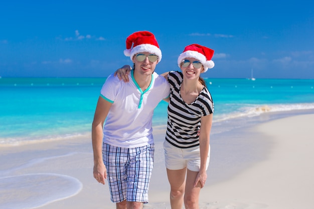 Jeune couple heureux en chapeaux rouges sur une plage tropicale