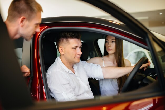 Un jeune couple heureux choisit et achète une nouvelle voiture chez un concessionnaire automobile. Acheter une nouvelle voiture.