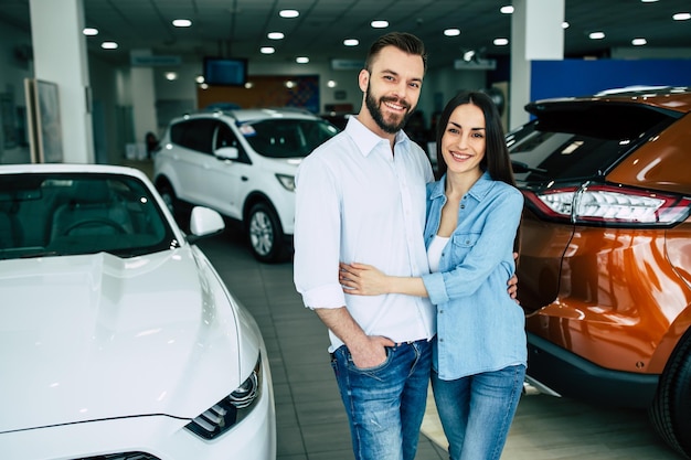 Un jeune couple heureux choisit et achète une nouvelle voiture pour la famille chez le concessionnaire