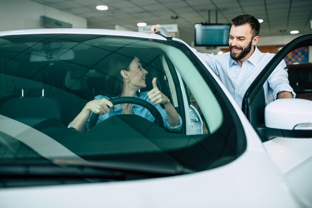 Un jeune couple heureux choisit et achète une nouvelle voiture pour la famille chez le concessionnaire