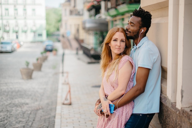 Jeune couple heureux, écouter de la musique avec des écouteurs dans une rue de la ville par une journée ensoleillée