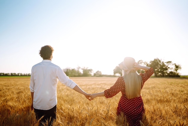 Jeune couple heureux étreignant sur un champ de blé au coucher du soleil Profitant du temps ensemble