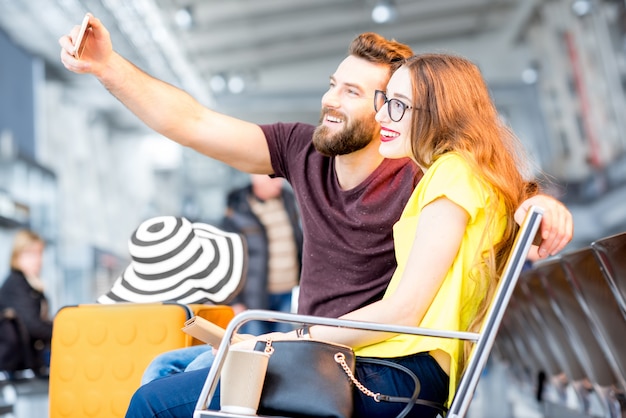 Jeune couple heureux faisant une photo de selfie avec un téléphone dans la salle d'attente de l'aéroport pendant leurs vacances d'été