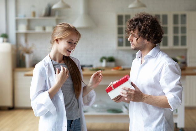 Jeune couple heureux à la maison, homme offrant un cadeau à sa petite amie et la rendant très heureuse. Donner des cadeaux.