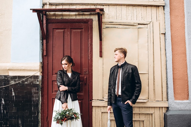 Jeune couple heureux marche dans une rue de la ville après la pluie. Jeunes mariés avec des vestes en cuir à l'extérieur. Mariage d'automne.