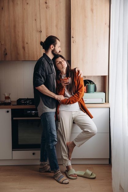 Un jeune couple heureux, mari et femme, s'embrassent paisiblement dans leur cuisine.
