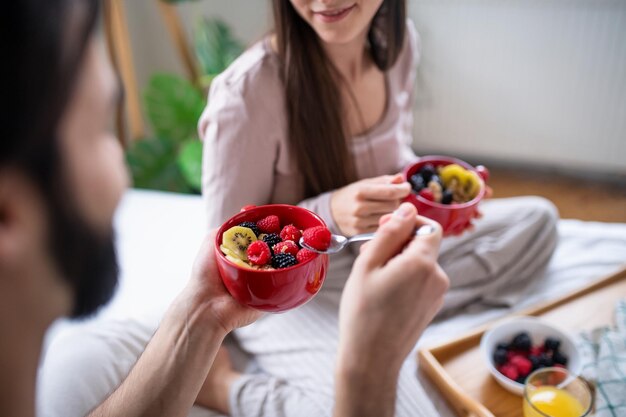 Jeune couple heureux méconnaissable amoureux mangeant le petit déjeuner sur le lit à l'intérieur à la maison.