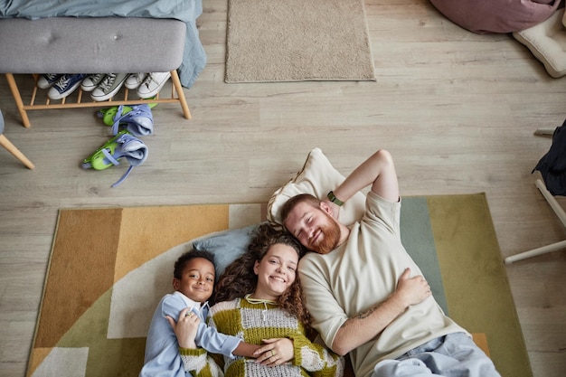 Un jeune couple heureux posant avec un enfant adopté allongé sur le sol dans la chambre des enfants
