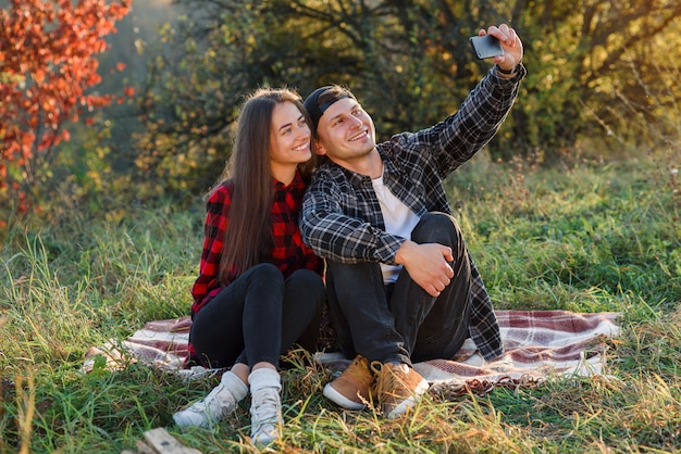 Jeune couple heureux prenant selfie à l'aide de smartphone dans le parc.