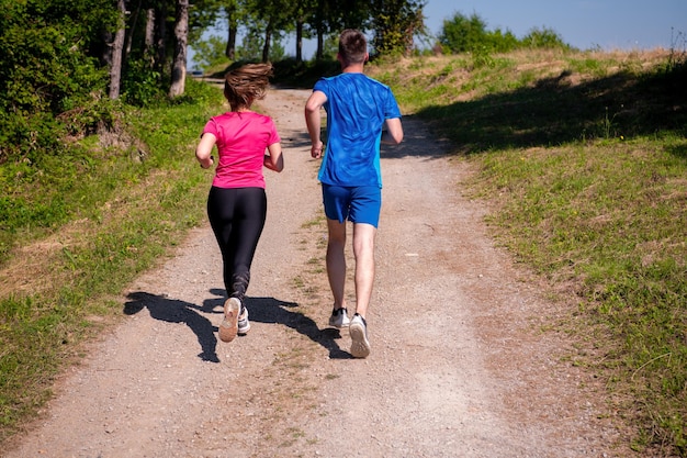 jeune couple heureux profitant d'un mode de vie sain tout en faisant du jogging sur une route de campagne à travers la belle forêt ensoleillée, l'exercice et le concept de remise en forme