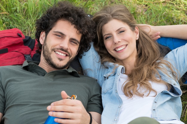 Jeune couple heureux reposant sur l'herbe en regardant la caméra