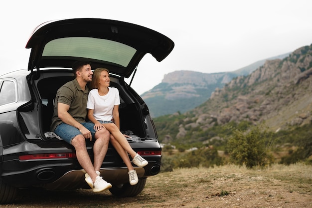 Jeune couple heureux sur un road trip assis dans le coffre de la voiture