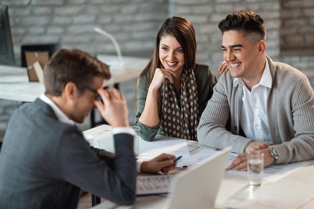 Jeune couple heureux s'amusant lors des consultations avec leur agent d'assurance au bureau