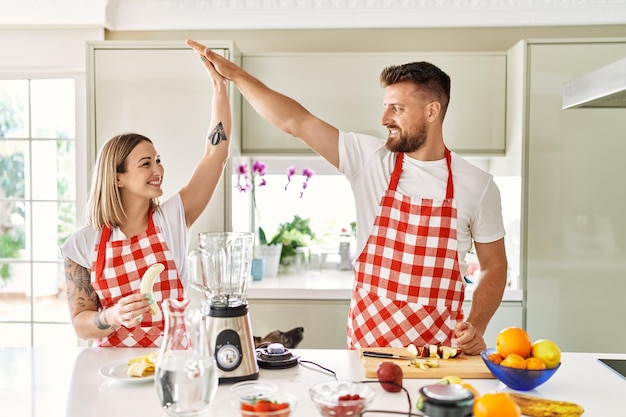 Jeune couple high five avec les mains levées faisant du smoothie à la cuisine