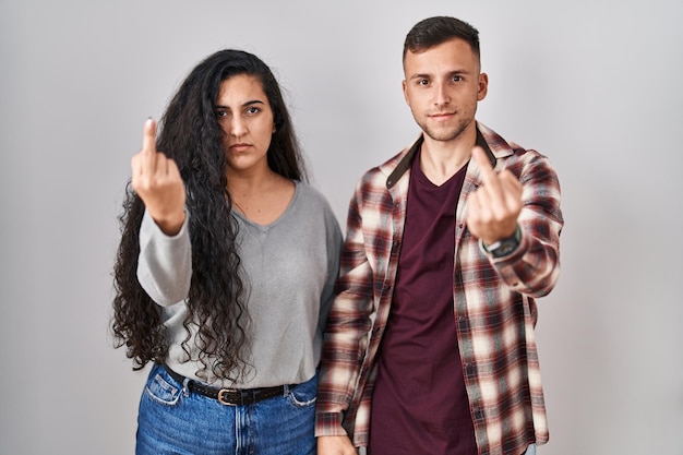 Jeune couple hispanique debout sur fond blanc montrant le doigt du milieu, expression de baise impolie et grossière