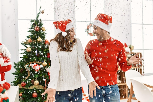 Jeune couple hispanique portant un chapeau de noël jetant des confettis célébrant le nouvel an à la maison.