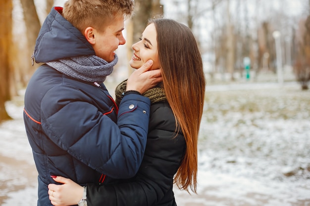 Un jeune couple en hiver vestes et foulards marchent dans un parc enneigé