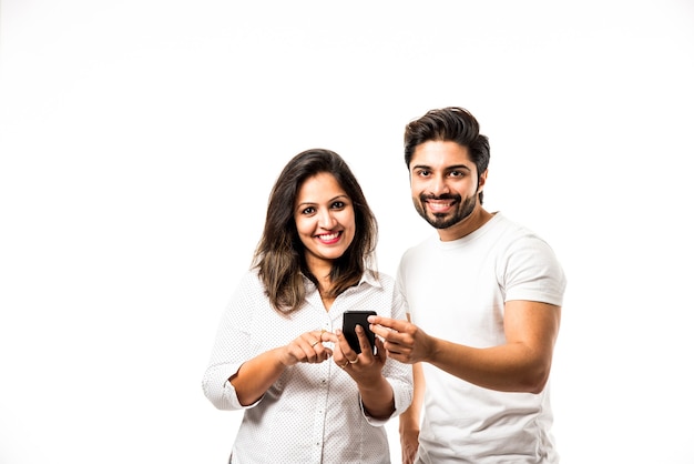 Jeune couple indien utilisant un smartphone ou un combiné mobile, isolé sur fond blanc ou sur fond de brique rouge