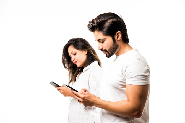 Jeune couple indien utilisant un smartphone ou un combiné mobile, isolé sur fond blanc ou sur fond de brique rouge