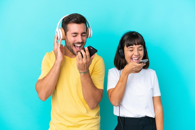 Jeune couple isolé sur fond bleu écoutant de la musique avec un mobile et chantant
