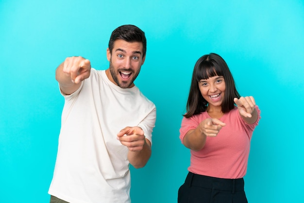 Jeune couple isolé sur fond bleu pointe le doigt vers vous en souriant