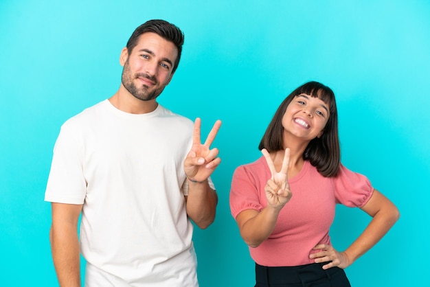 Jeune couple isolé sur fond bleu souriant et montrant le signe de la victoire