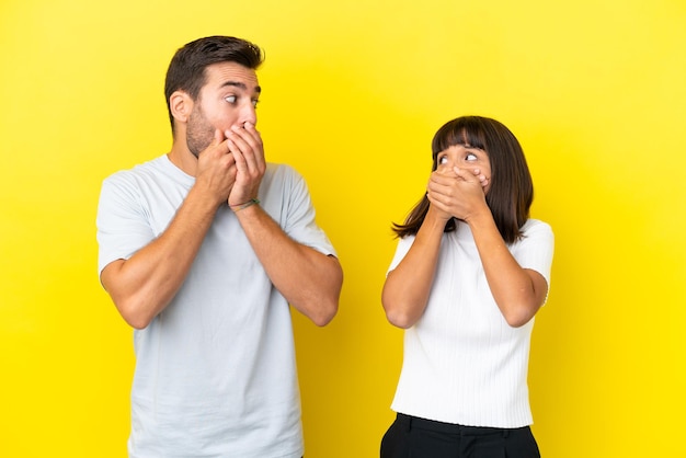 Jeune couple isolé sur fond jaune couvrant la bouche avec les mains pour dire quelque chose d'inapproprié