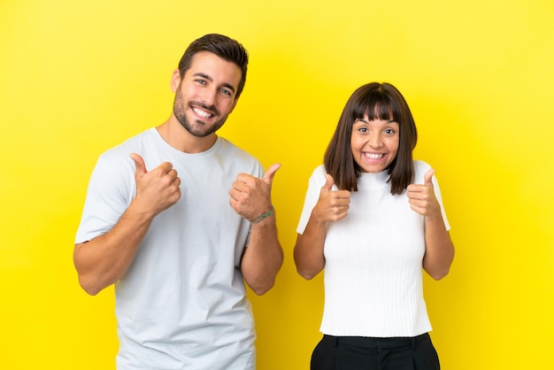 Jeune couple isolé sur fond jaune donnant un coup de pouce geste avec les deux mains et souriant