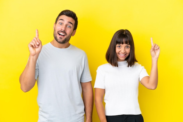 Jeune couple isolé sur fond jaune montrant et levant un doigt en signe du meilleur