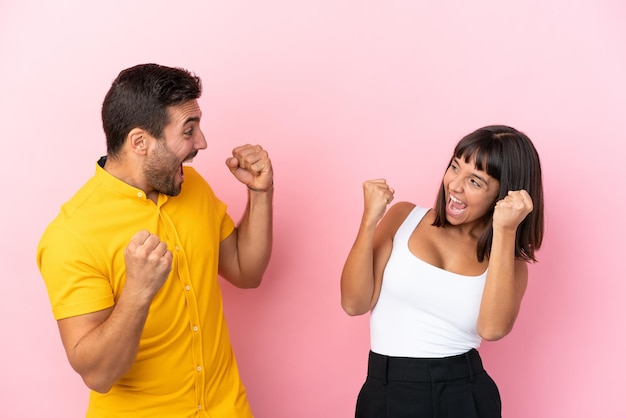 Jeune couple isolé sur fond rose célébrant une victoire en position de vainqueur