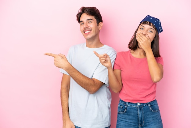 Jeune couple isolé sur fond rose doigt pointé sur le côté en position latérale