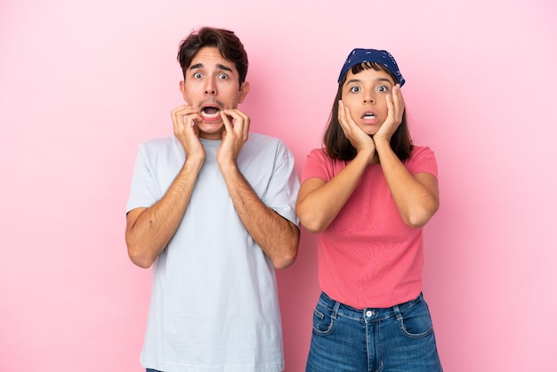 Jeune couple isolé sur fond rose surpris et choqué en regardant à droite