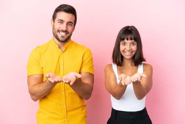 Jeune couple isolé sur fond rose tenant un fond imaginaire sur la paume pour insérer une annonce