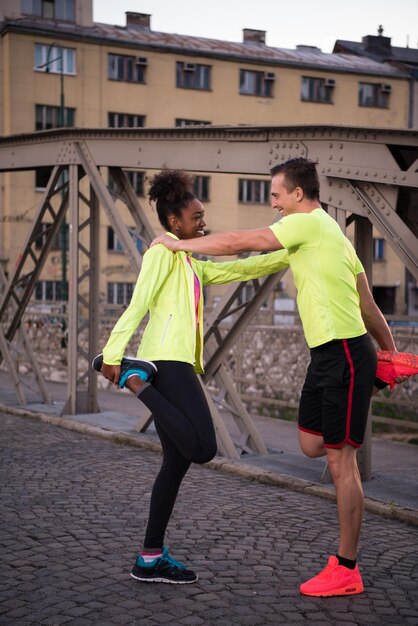 Photo jeune couple de jogging multiethnique s'échauffant et s'étirant avant de courir le matin dans la ville