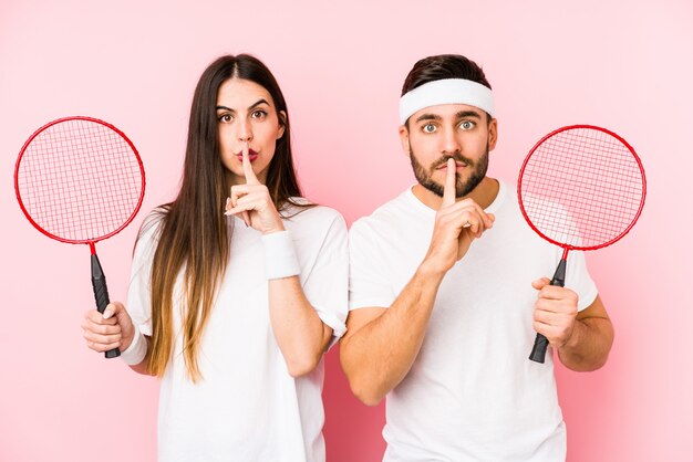 Jeune couple jouant au badminton isolé en gardant un secret ou en demandant le silence.