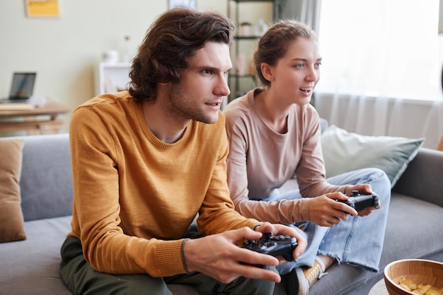 Un jeune couple jouant à des jeux vidéo ensemble et tenant des contrôleurs