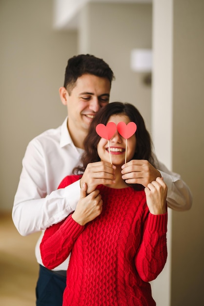 Jeune couple joyeux amoureux tenant des coeurs rouges sur les yeux et souriant
