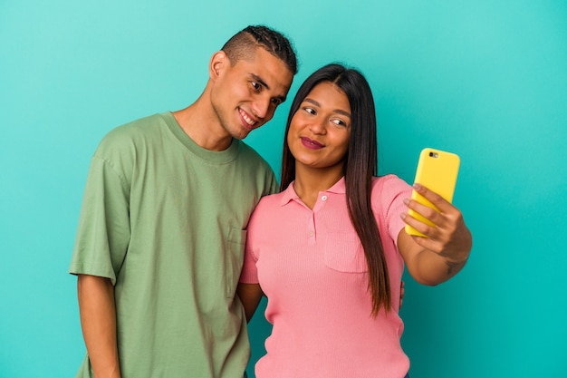 Jeune couple latin avec un téléphone portable isolé sur un mur bleu